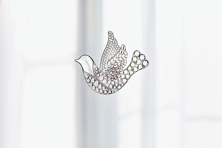 Souvenir glass dove, symbol of peace and spring. Figurine of a bird in flight Dove transparent. A beautiful sign of spring. With copy space. Glass toy on the background of a windowの写真素材