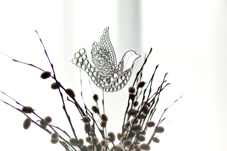 Souvenir glass dove, symbol of peace and spring. Figurine of a bird in flight dove clear of willow branches. A beautiful sign of spring. With copy space. Glass toy on the background of a windowの写真素材
