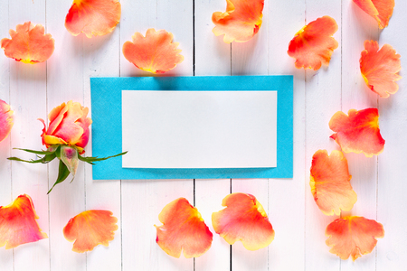 Romantic pearl blue envelope with space for a signature on a white wooden background. With copy space. Pink rose petals around the envelope. Letter to the recognition of love.の写真素材