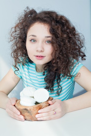 Portrait of a young girl with brown curly hair. It keeps holding vase with white marshmallows. Eastern sweetness. Gentle and dreamy look. Good morning. Dessert for breakfastの写真素材