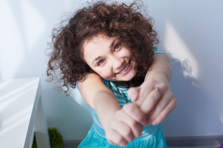 Portrait of a beautiful young girl with brown curly hair. Fun and joy. Happy girl in the morning sun is smiling at the camera. Delicate blue dress.の写真素材