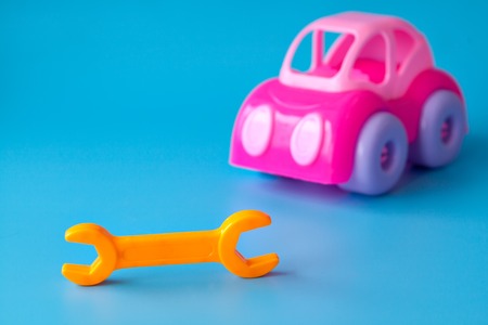 Pink toy car made of plastic on a blue background. Toy wrench orange. Playing in the car repair shop. Copy space.の写真素材