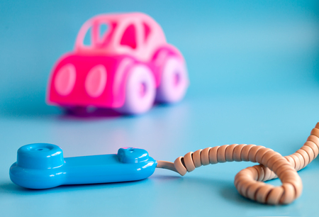 Pink toy car made of plastic on a blue background. Plastic toy phone. Playing in car repairs. Call mechanic and repair the machine. Copy space.の写真素材