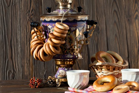Still life with traditional Russian samovar with bagels and bagels with a cup of tea on wooden background. Traditional golden samovar and a sprig of mountain ash on a napkin in a cage.の写真素材