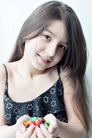 Portrait of a little girl with dark long hair holding a large handful of colorful candies. Happy smiling baby.の写真素材