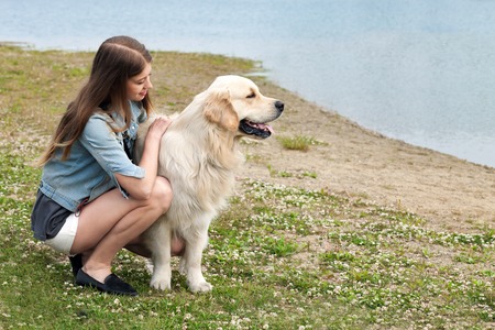 Portrait of a young girl and her dog golden retriever outdoors in the summer. On the bank of the riverの写真素材