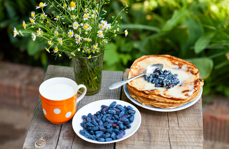 Bouquet of daisies, pancakes with berries and a glass of milk on a wooden table close-up view from above. Pancakes and milk for breakfast.の写真素材