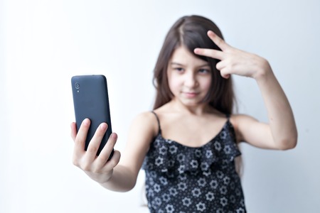 Charming little girl photographed themselves on the smart phone and various posesの写真素材
