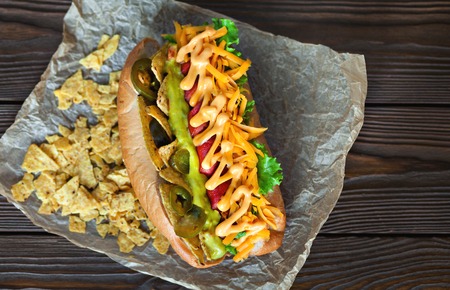 Big tasty hot dog with sausage, vegetables isousom on parchment on the wooden background. hot dogs to gourmet.の写真素材