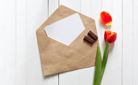 Spring bouquet of red tulips and a card in an envelope on a white wooden background with copy space. View from the top with space for signature.の写真素材