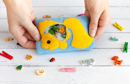 Children's toy made of colored fleece for the development of motor skills in the hands of women. Bag with yellow fish fleece filled with plastic beads and figurines on a white wooden background. handmade toys. Happy childhood.の写真素材