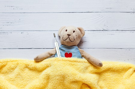 children's soft toy teddy bear in bed with thermometer and pills, take the temperature of a mercury...