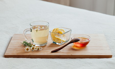 Herbal tea in glass cup with flowers of chamomile, turmeric and honey on a wooden board. Treatment of hot drink. Treatment of folk remedies in bed.の写真素材