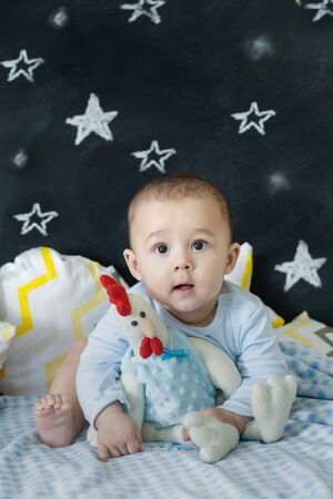 Cheerful toddler on a bed hugging a chicken stuffed toy. Vertical indoors shotの写真素材
