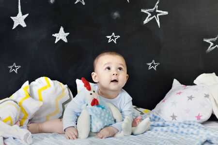 Cheerful toddler on a bed hugging a chicken stuffed toy. Vertical indoors shotの写真素材