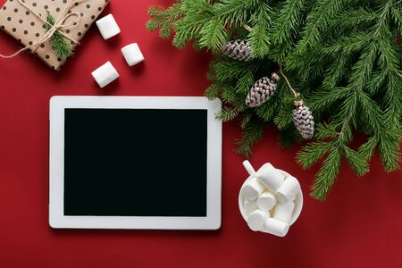 Christmas composition. Christmas decorations, gadget and beverage, fir branches on a red background. Flat lay, top view, copy spaceの写真素材