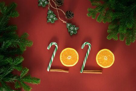 Christmas composition. Figures 2020 made of candy and half oranges. Branches of spruce on a red background. Christmas presents, winter, new year concept. Flat lay, top view, copy spaceの写真素材