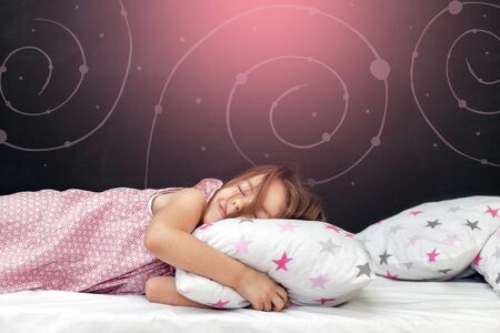Charming little girl of preschool age sleeps in bed on a pillow with stars. Time to sleep. Abstract background about space and the dreams of a child. Pink dreams.の写真素材