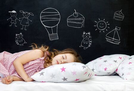 Charming little girl of preschool age sleeps in bed on a pillow with stars. Time to sleep. Drawing about the dreams of a child: kitten, dessert, adventure and friendship.の写真素材