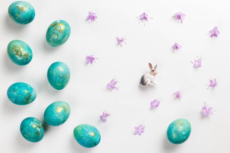 Happy easter card. Stylish minimalistic composition of turquoise with gold easter eggs on a white background. Figurine of a rabbit and delicate spring flowers. Flat lay, top view, copy spaceの写真素材