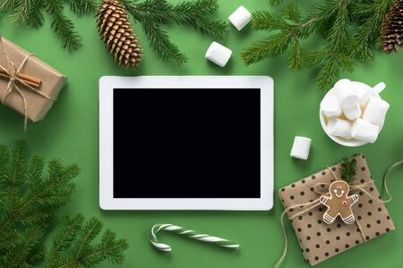 Christmas composition. Christmas decorations, tablet and marshmallows, branches of spruce on a green background. Flat lay, top view, copy spaceの写真素材