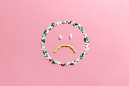 Composition of pills and capsules on a pink background in the form of emoji. Sad emotions. Psychological help. Copy space. View from above. Flat lay.の写真素材
