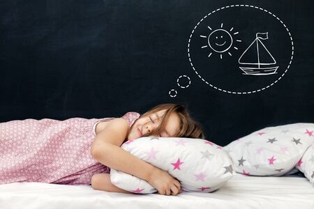 Charming little girl of preschool age sleeps in bed on a pillow with stars. Time to sleep. Drawing about the dreams of a child. Copy spaceの写真素材