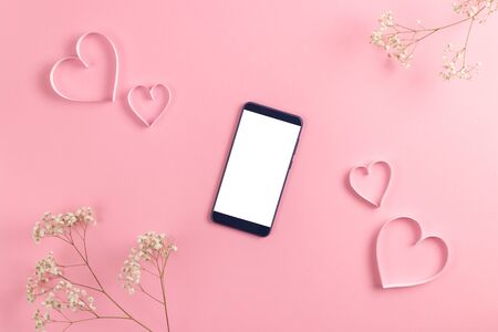 Composition for Valentines Day February 14th. Delicate pink background, phone and notebook with recognition. A heart cut out of paper. Greeting card. Flat lay, top view, copy space.の写真素材