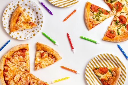 Pieces of pizza and colored candles for a cake on a white background. Birthday with junk food. Children's party. Top view with copy space for text. Flat lay.の写真素材