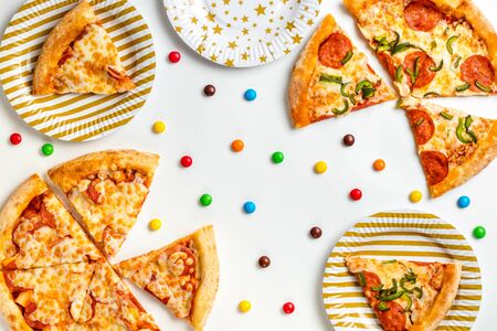 Pieces of pizza and colored sweets on a white background. Birthday with junk food. Children's party. Top view with copy space for text. Flat lay.の写真素材
