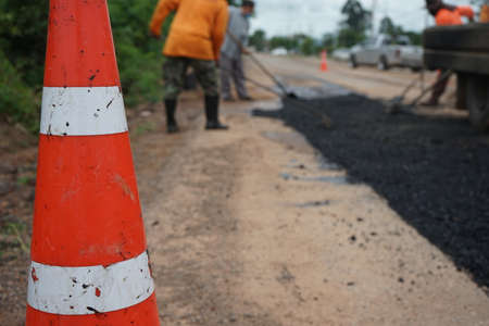 A blur of road maintenance work and an orange cone in the front.の写真素材