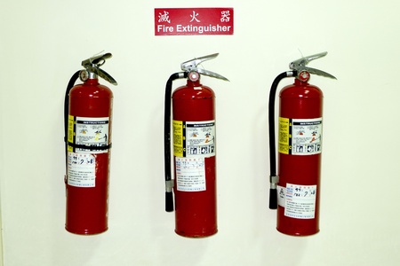 three fire extinguishers in row on white wallの写真素材