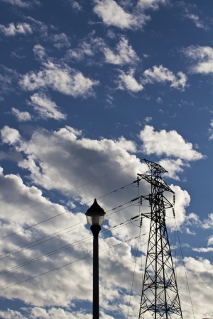 silhoutted electric high voltage power post against blue cloudy skyの写真素材