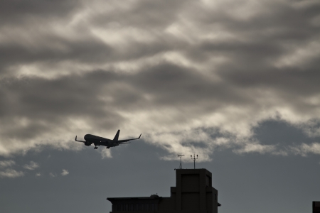 silhoutted airplane flying in the cloudy sky above a cityの写真素材