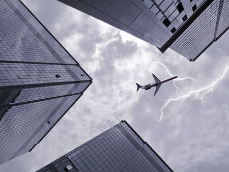 Bottom view of airplane flying above skyscraper in stormy skyの写真素材