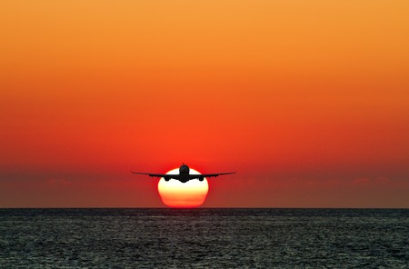 silhoutted business passenger airplane in the air against sun