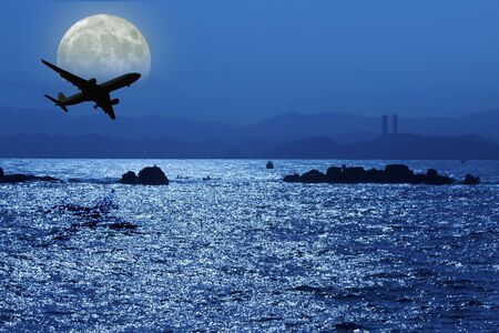airplane fly above ocean under moonlightの写真素材