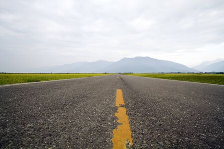 asphalt road through the green field on cloudy sky in winter dayの写真素材