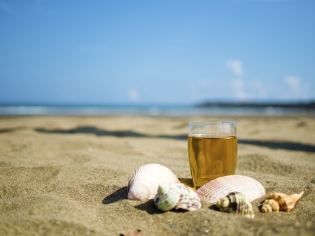 glass of tea with shells on summer beachの写真素材