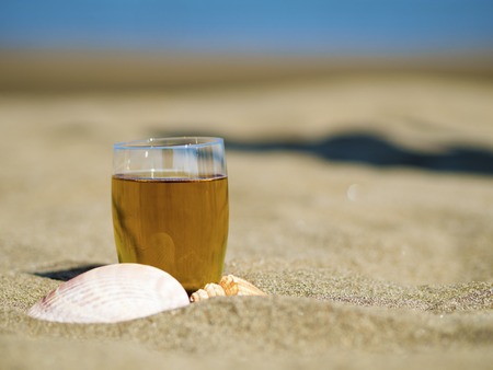 glass of tea with shells on summer beachの写真素材