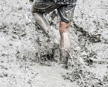 A participant of a physically demanding run, runs through the mud