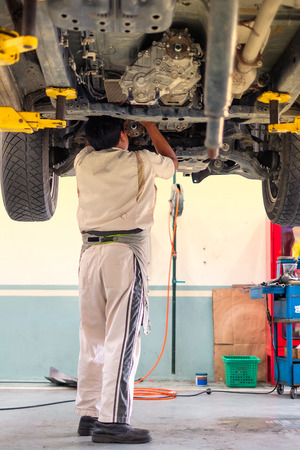 An auto mechanic standing under the car that is on lifting platform, car repairの写真素材
