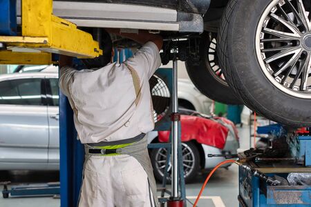 An auto mechanic standing under the car that is on lifting platform, car repairの写真素材