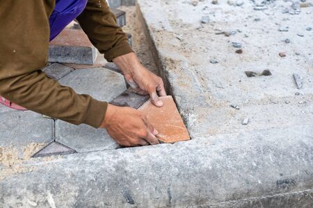Close-up of hands of worker working on placing stone block for foot path.の写真素材