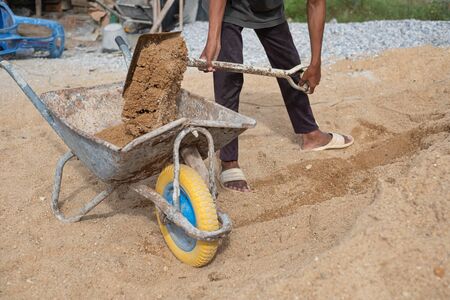 A worker use the shovel to fill the sand into the wheelborrow for construction of new house. Construction toolsの写真素材