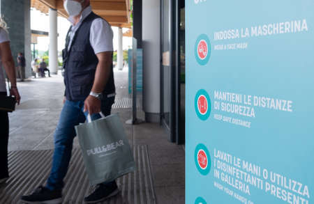 Italy, Milan, 05/31/2020, people walk wearing surgical mask due to the social distance for coronavirus covid. in the foreground a sign with the safety indications for social distancing, hygiene and safetyのeditorial素材