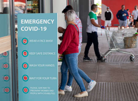 Italy, Milan, 05/31/2020, people walk wearing surgical mask due to the social distance for coronavirus covid. in the foreground a sign with the safety indications for social distancing, hygiene and safetyのeditorial素材