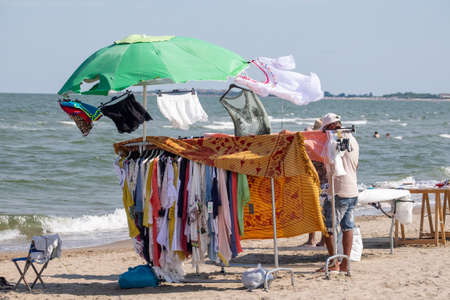 Italy, Chioggia, 06/25/2020. african street vendor dressed in white, on the beach sells various itemsのeditorial素材