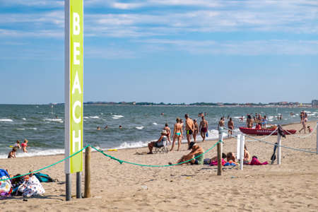 Italy, Chioggia, 06/25/2020, tourists on the beach. Next to it a green sign with Beach writing. Focus on main subject green road signのeditorial素材