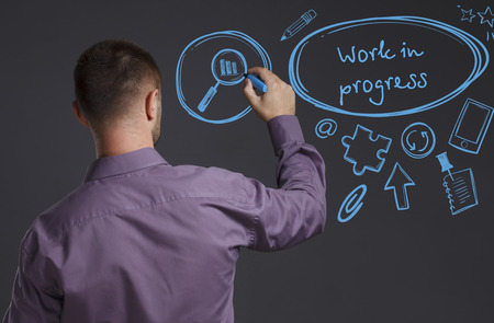 Business, Technology, Internet and network concept. A young businessman writes on the blackboard the word: Work in progressの写真素材